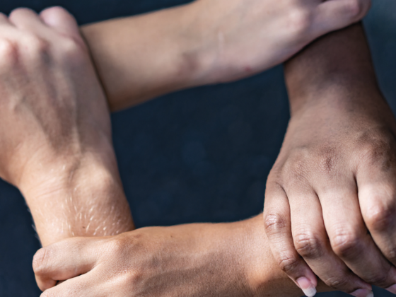 A photo of four hands holding one another's wrists in a linked square