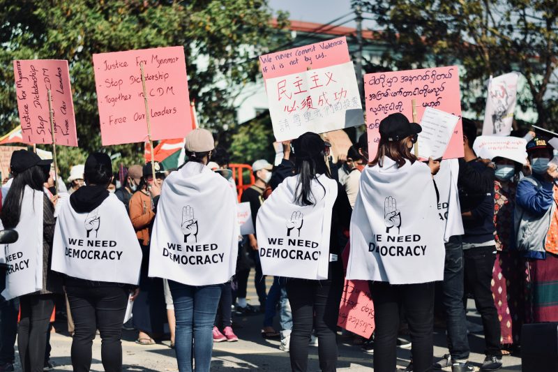 A group of protesters in Myanmar holding signs saying "We need democracy"